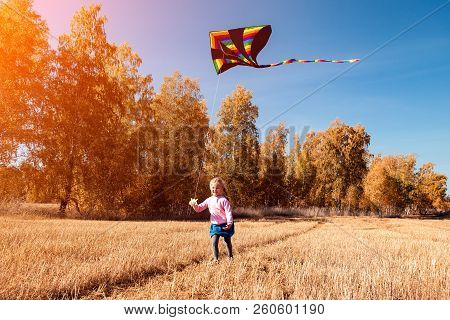 A Small Cheerful Girl With Blond Hair Smiles, Enjoys Nature And Plays With A Kite On A Warm Autumn S