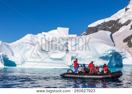 Boat Full Of Tourists Explore Huge Icebergs Drifting In The Bay Near Cuverville Island, Antarctic Pe