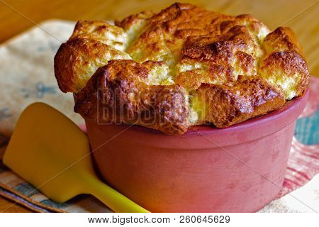 Homemade Cheese Souffle In A Clay Souffle Pot With A Yellow Spatula.