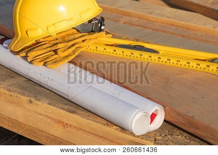 Abstract of Constrcution Hard Hat, Gloves, Level and House Plans Resting on Wood Planks.