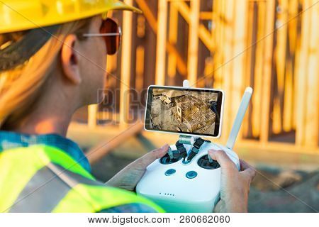 Female Unmanned Aircraft System (UAV) Quadcopter Drone Pilot with Controller Inspecting New House Framing.