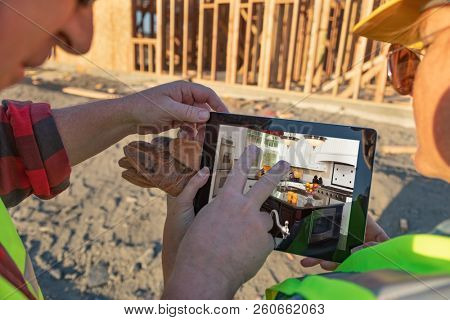 Male and Female Construciton Workers Reviewing Kitchen on Computer Pad at Construciton Site.