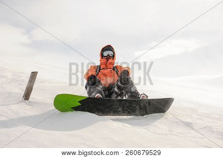 Male Snowboarder Dressed In Orange Sportswear Riding Down The Mountain Hill On The Board On Cloudy D