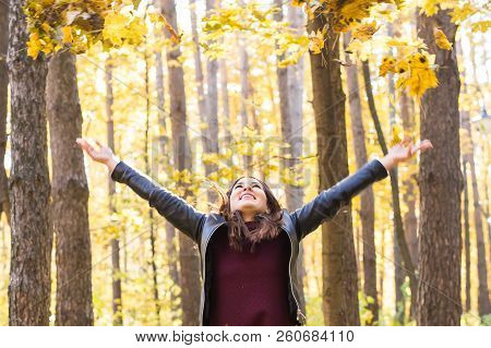 Autumn, Joy And People Concept - Young Woman Having Fun In Autumn Park. She Is Throwing Yellow Leave