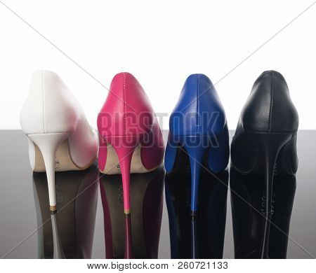 Black, Blue Pink And White High Heels Pointed Woman Shoes On The Back And Heels On Reflective Floor.