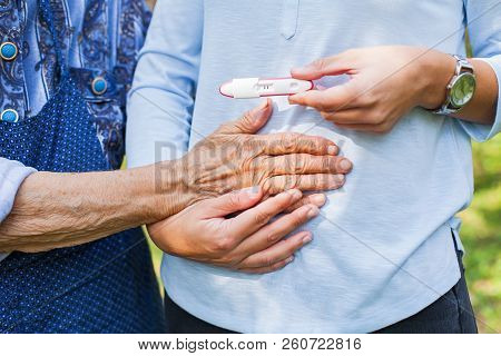 Close Up Picture Of Young Woman Holding Pregnancy Test With Grandmother. Great-grandchild On The Way