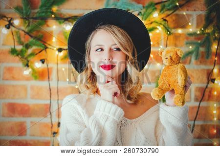 Portrait Of A Young Cozy Woman In White Sweater With Teddy Beartoy And Christmas Lights On Backgroun