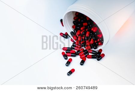 Red, Black Capsules Pill Spilled Out From White Plastic Bottle Container. Antibiotics Drug Resistanc