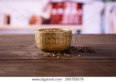 Lot Of Whole Fresh Brown Flaxseeds With Wooden Bowl With Grey Kitchen In Background