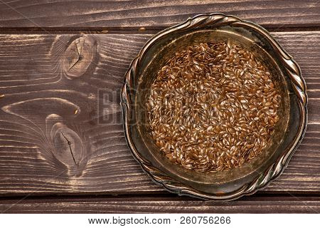 Lot Of Whole Fresh Brown Flaxseeds In Old Iron Bowl Flatlay On Brown Wood