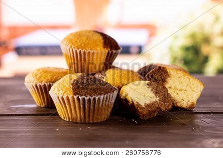Group Of Four Whole Two Halves Of Fresh Baked Marble Muffin With Books Near The Window In Background