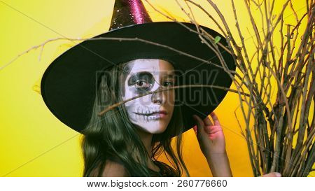 Halloween, Girl With Make-up Skeleton On Half Face, Dressed As Witch, Posing On Bright Yellow Backgr