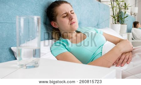 Portrait Of Young Woman Lying In Bed And Suffering From Pain In Stomach
