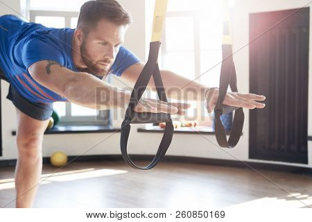 Portrait Of Handsome Man Athlete Doing Exercise Alone With Fitness Belts In Modern Gym Club, Workout