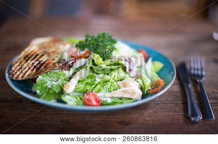 Fresh Caesar Salad In Blue Plate On Dark Wooden Table With Cuttlery Aside