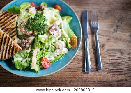 Fresh Caesar Salad In Blue Plate On Dark Wooden Table With Cuttlery Aside