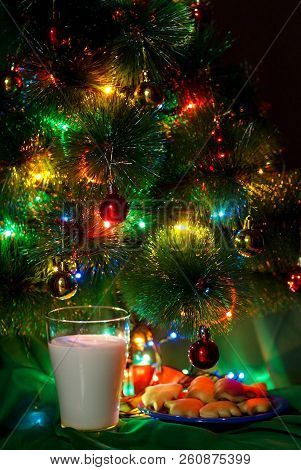A Glass Of Milk And A Slide Of Cookies On A White Plate For Santa Claus At The Christmas Tree Decora