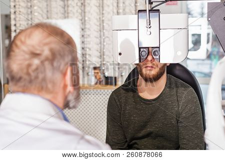 Ophthalmologist Examining Young Man With Optometric Machine In Optics Store