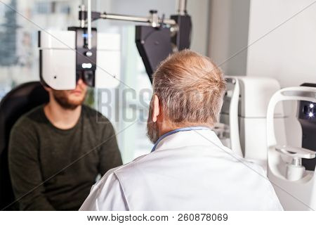 Ophthalmologist Examining Young Man With Optometric Machine In Optics Store