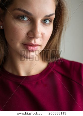 Fashion photo of a beautiful smiling brunette woman in a red sweater posing over gray empty background.