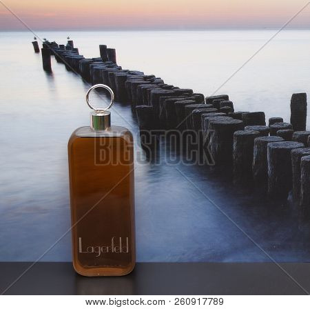 Lagerfeld, Mens Fragrance, Large Perfume Bottle In Front Of The Picture Of A Groyne In The Sea