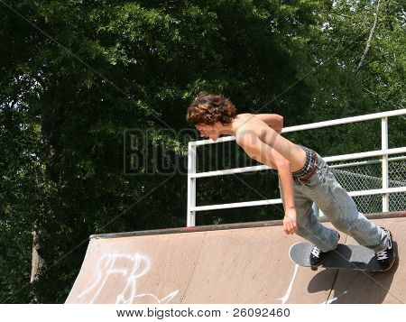 Teen boy shirtless in jeans skateboarding a skatepark all'aperto.