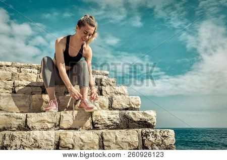 Women runner bootlace on her boot after running in sunny day under sunlight from blue sky near the sea.
