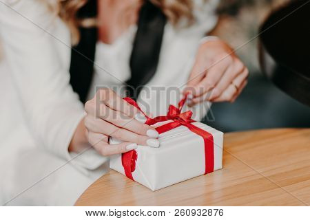 Photo Of Unrecognizable Caucasian Woman Ties Red Ribbon On Small White Gift Box, Prepares Surprise F