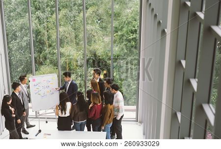 Businessman Presenting At Whiteboard Gruop Of Business People Standing Around White Board During Mee