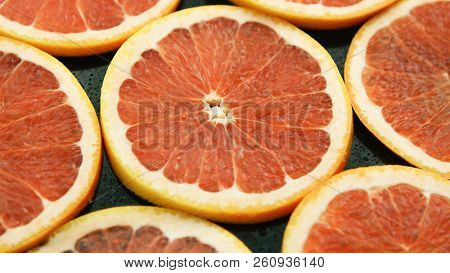 Closeup of composed round slices of cut grapefruit of bright ret color arranged together on glass surface