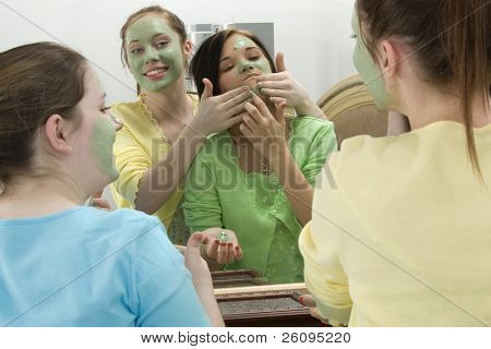 Três meninas adolescentes no espelho do quarto colocar máscara facial.  Concentrar-se na reflexão de menina em amarelo.