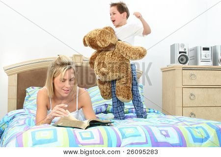 Máma čítanka pro syna, zatímco si hraje s obří vycpaný medvěd v posteli.