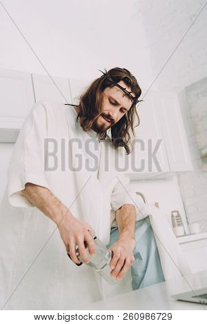 Low Angle View Of Jesus Grinding Coffee Beans With Hands In Manual Coffeemill In Kitchen At Home
