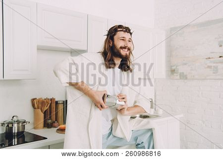 Smiling Jesus Grinding Coffee Beans With Hands In Manual Coffeemill In Kitchen At Home