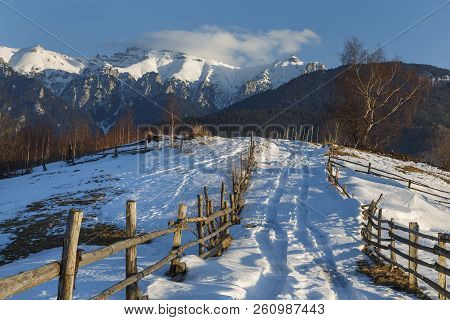 Alpine Scenery With Rustic Wooden Cottage And Snow Capped Ridge Of The Bucegi Mountains In The Sunse