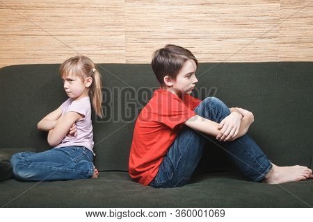 Frustrated siblings sittng on sofa stuck at home being in self-isolation. Quarantine and lockdown protective measures against spreading of coronavirus pandemic disease