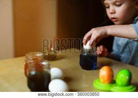 Todder Girl Sitting At The Table And Dipping An Egg In Food Paint Making Easter Decoration