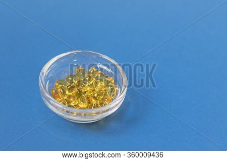 Yellow Gelatin Capsules With Vitamin D3 In A Glass Container On A Blue Background. Pharmaceutical Th
