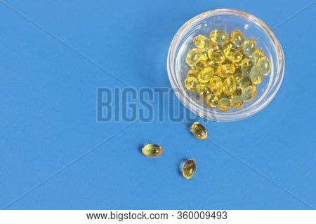 Yellow Gelatin Capsules With Vitamin D3 In A Glass Container On A Blue Background. Pharmaceutical Th
