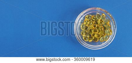 Yellow Gelatin Capsules With Vitamin D3 In A Glass Container On A Blue Background. Pharmaceutical Th
