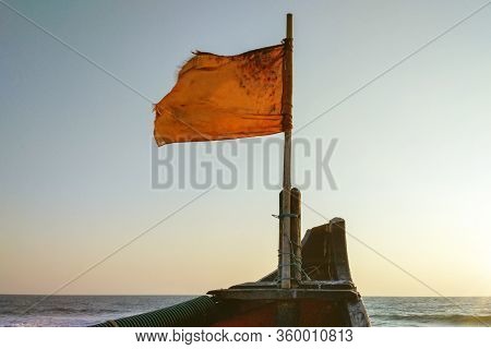 The Battered Flag At The Bow Of The Boat Flutters Against The Background Of The Sea And The Setting 