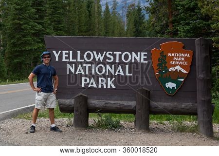 Yellowstone National Park,  Montana, Usa - July 13, 2014:  A Young Tourist Stands By A Wooden Sign F