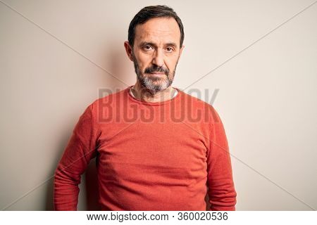 Middle age hoary man wearing casual orange sweater standing over isolated white background Relaxed with serious expression on face. Simple and natural looking at the camera.