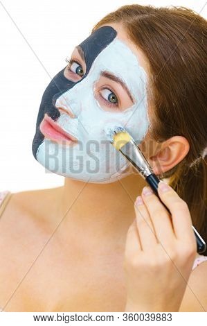 Woman With Clay Carbo Black Mask On Half Face Applying White Mud To Clean Skin. Girl Taking Care Of 