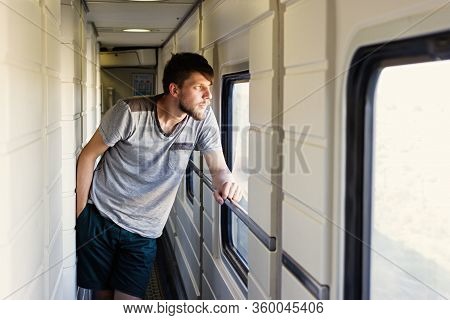 Handsome Young Caucasian Man With A Beard, Looks Outside Of The Train's Window, Looking At The Lands