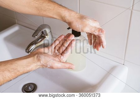 Man Cleaning His Hands Using Liquid Disinfectant Soap And Water In Bathroom.