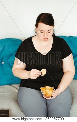 Overeating And Gluttony Concept. Mindless Snacking, Home Sedentary Lifestyle. Obese Woman Sitting On