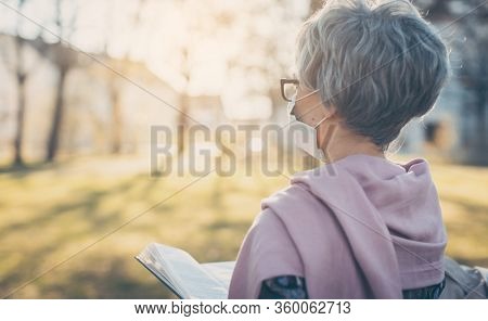 Senior lady praying with face mask reading the bible in front of a church in Covid-19 times