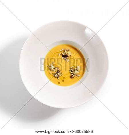 Pumpkin soup in white bowl. Served main course top view. Vegetable cream soup decorated with seeds. Restaurant food portion, main course. Vegetarian supper. Dinner, gourmet meal in plate