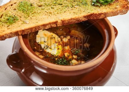 Oven baked meat soup with artichokes in pot. Delicious hot pottage with fresh bread and greenery. Traditional cuisine, restaurant dish, dinner food. Aromatic goulash on white napkin